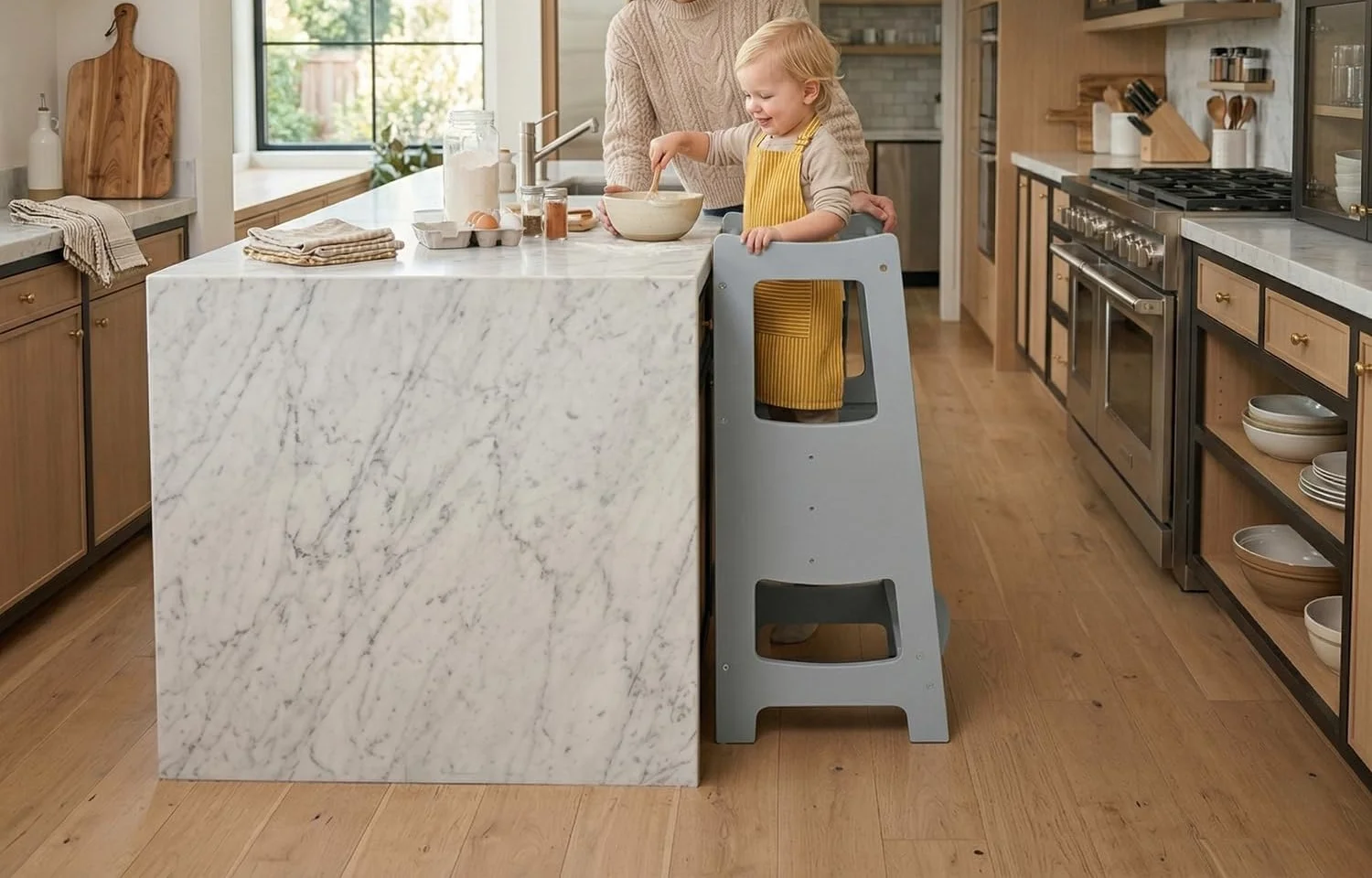 A toddler standing in a grey wooden kitchen tower at a marble island